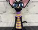Handmade crochet black sphynx cat plush wearing glasses and a purple and yellow striped sweater